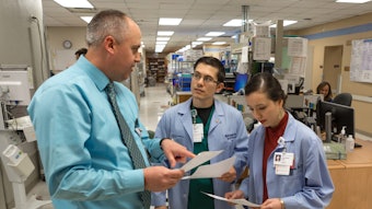 Man in a tie talking to two medical professionals in scrubs.