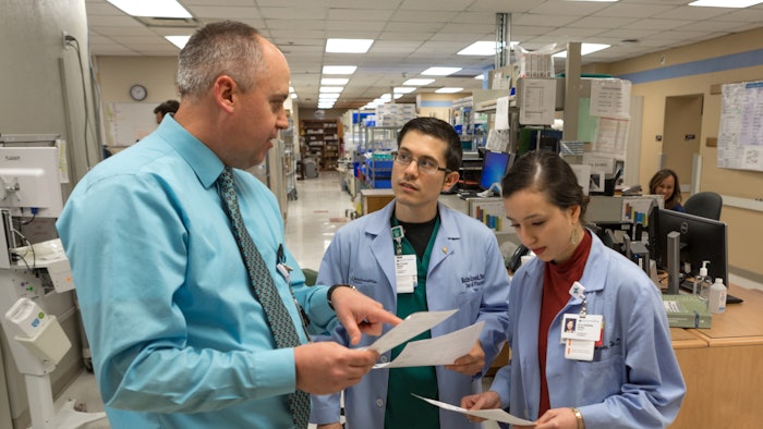 Man in a tie talking to two medical professionals in scrubs.