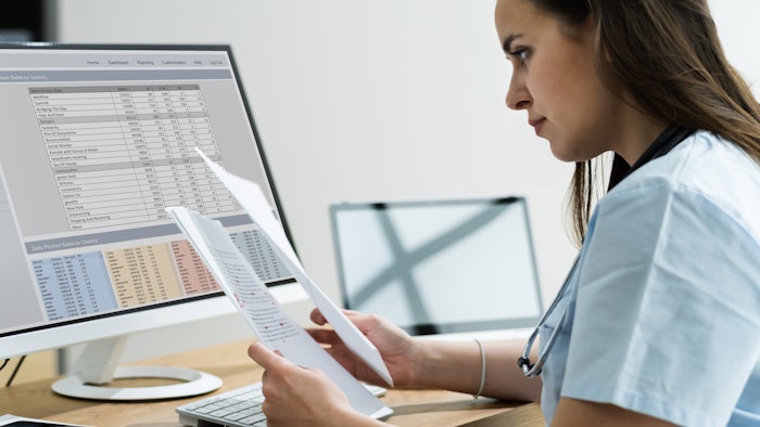 medical professional looking at papers in front of computer screen