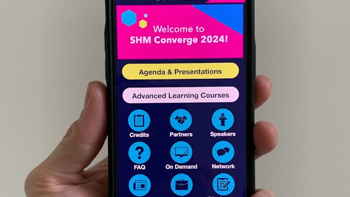 Hand holding a phone displaying the SHM Converge app