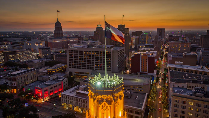 Aerial photo taken over a building with a Texas Flag in downtown San Antonio, Texas during sunset.