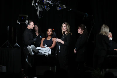 Multiple male and female dermatologists assess cosmetic needs on the face of a Black woman.