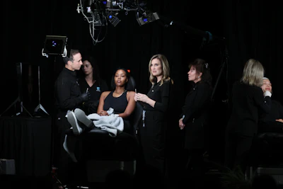Multiple male and female dermatologists assess cosmetic needs on the face of a Black woman.