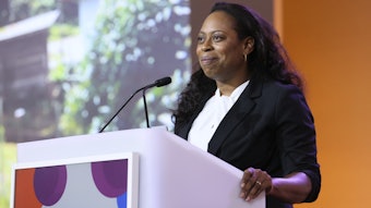 This is a photo of a Black female dermatologist speaking at a podium during an AAD meeting.