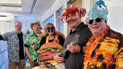 Harry (far right) and the IT team brought their competitive spirit to the 2024 staff Halloween Decorating Contest with travel theme “Cheeseburger in Paradise”.