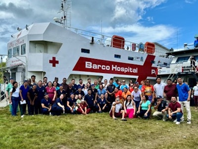 The amazing healthcare team of the Pope Francis Hospital Ship stands in front of the main ship.