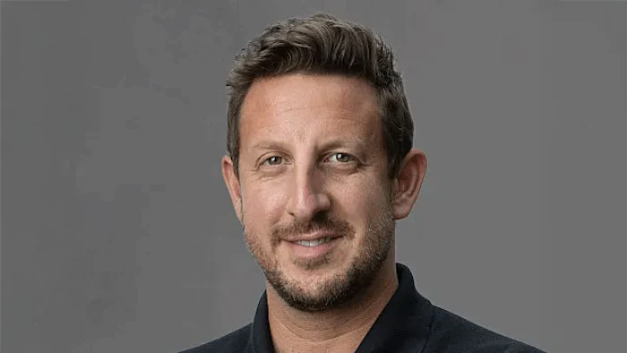 Professional headshot of a smiling man in a black shirt against a gray background