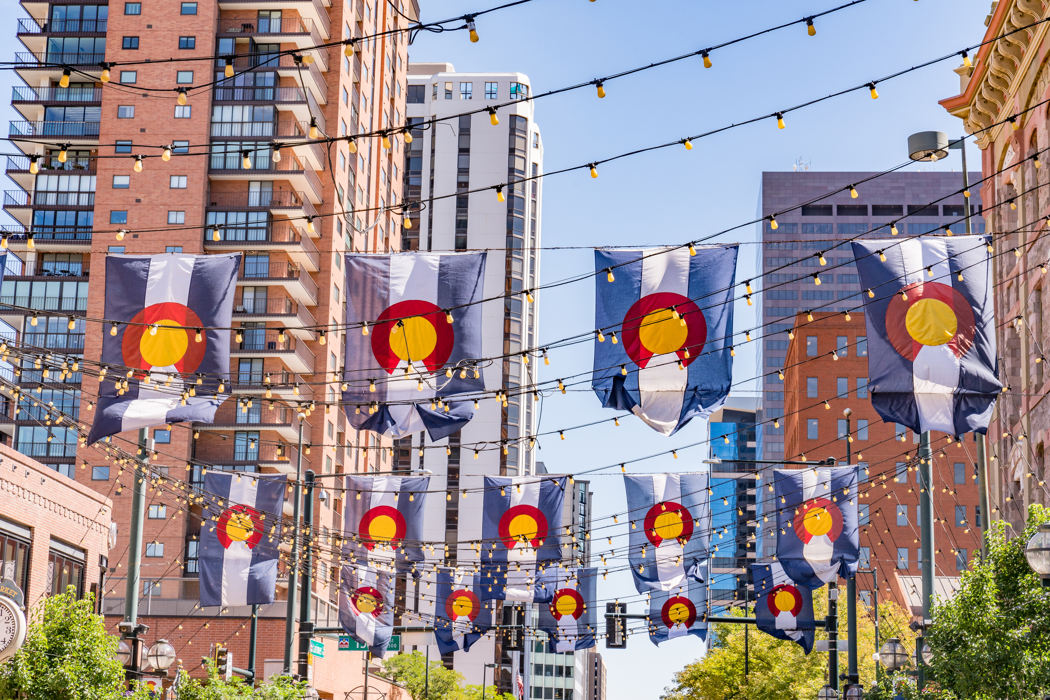 Colorado state flags hanging on downtown street with festive lights