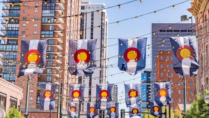 Colorado state flags hanging on downtown street with festive lights
