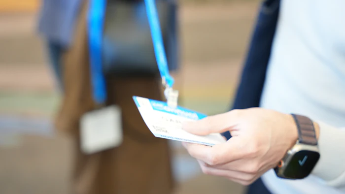 Conference badge with blue lanyard held by hand wearing watch