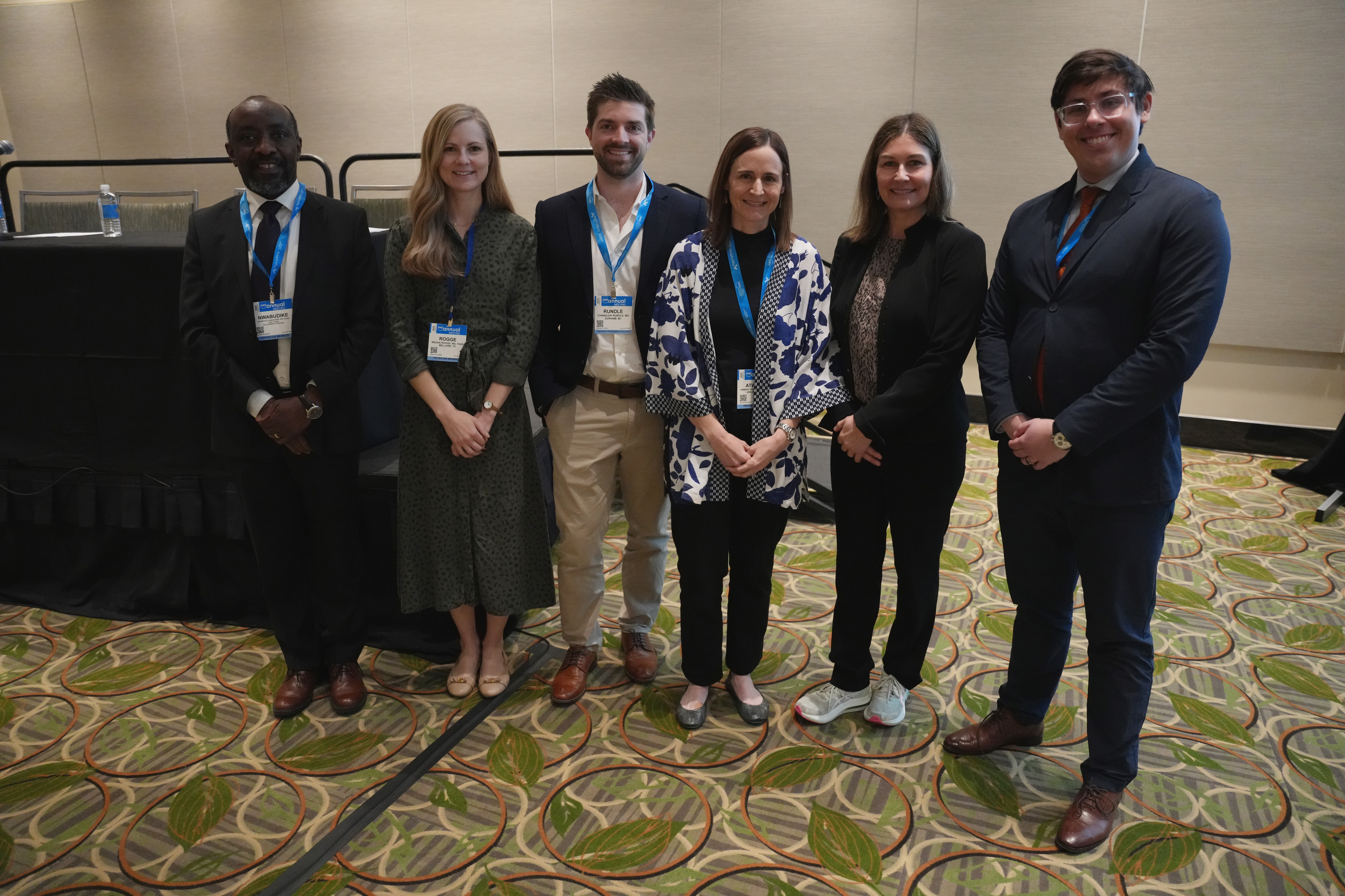 Six professionals standing together at a conference, wearing business attire and name badges