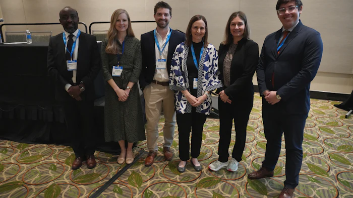 Six professionals standing together at a conference, wearing business attire and name badges