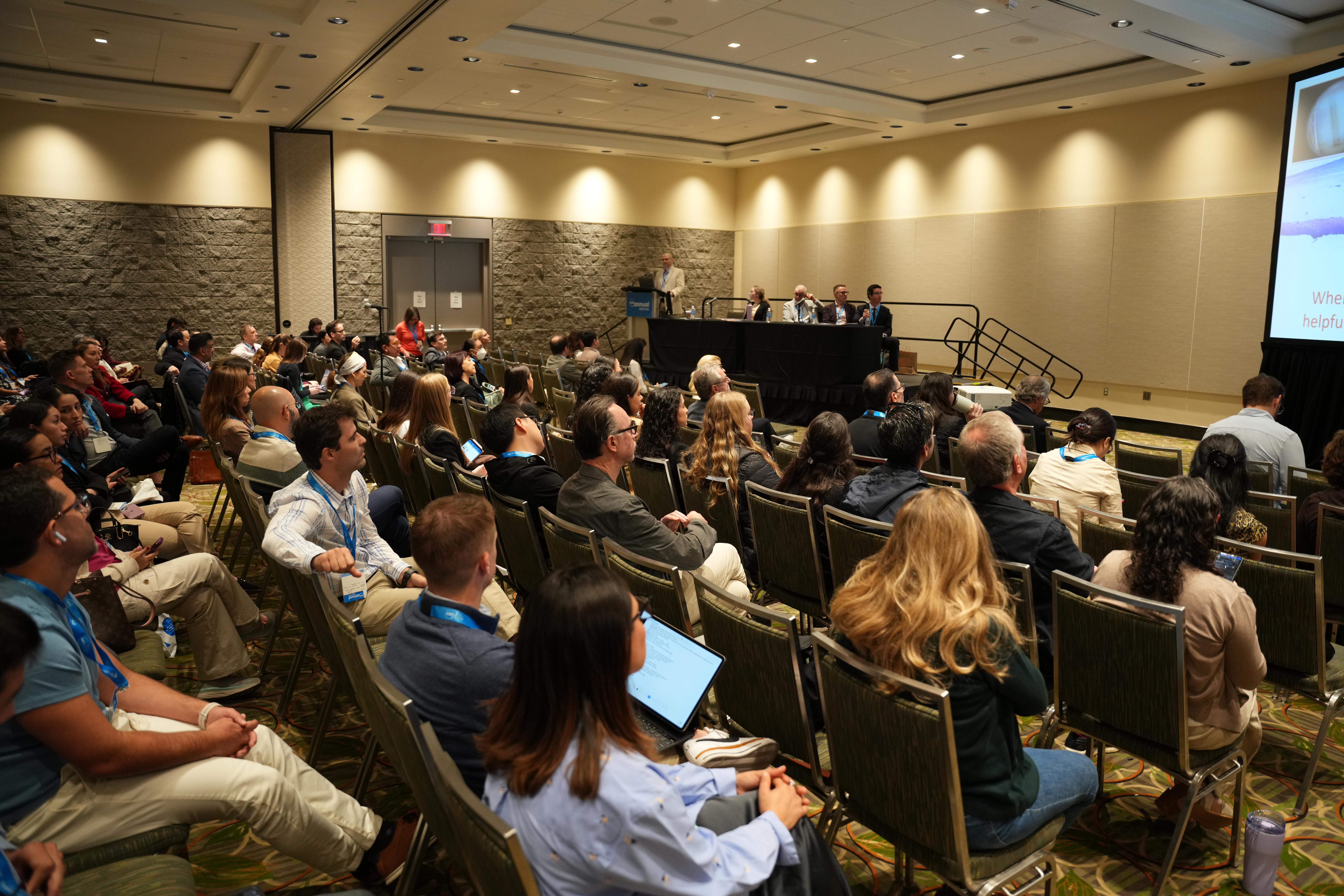 Conference room with attendees seated, listening to panel discussion at front stage