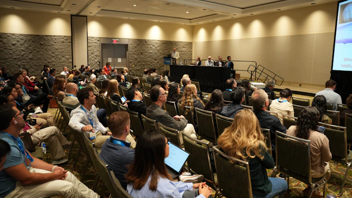 Conference room with attendees seated, listening to panel discussion at front stage