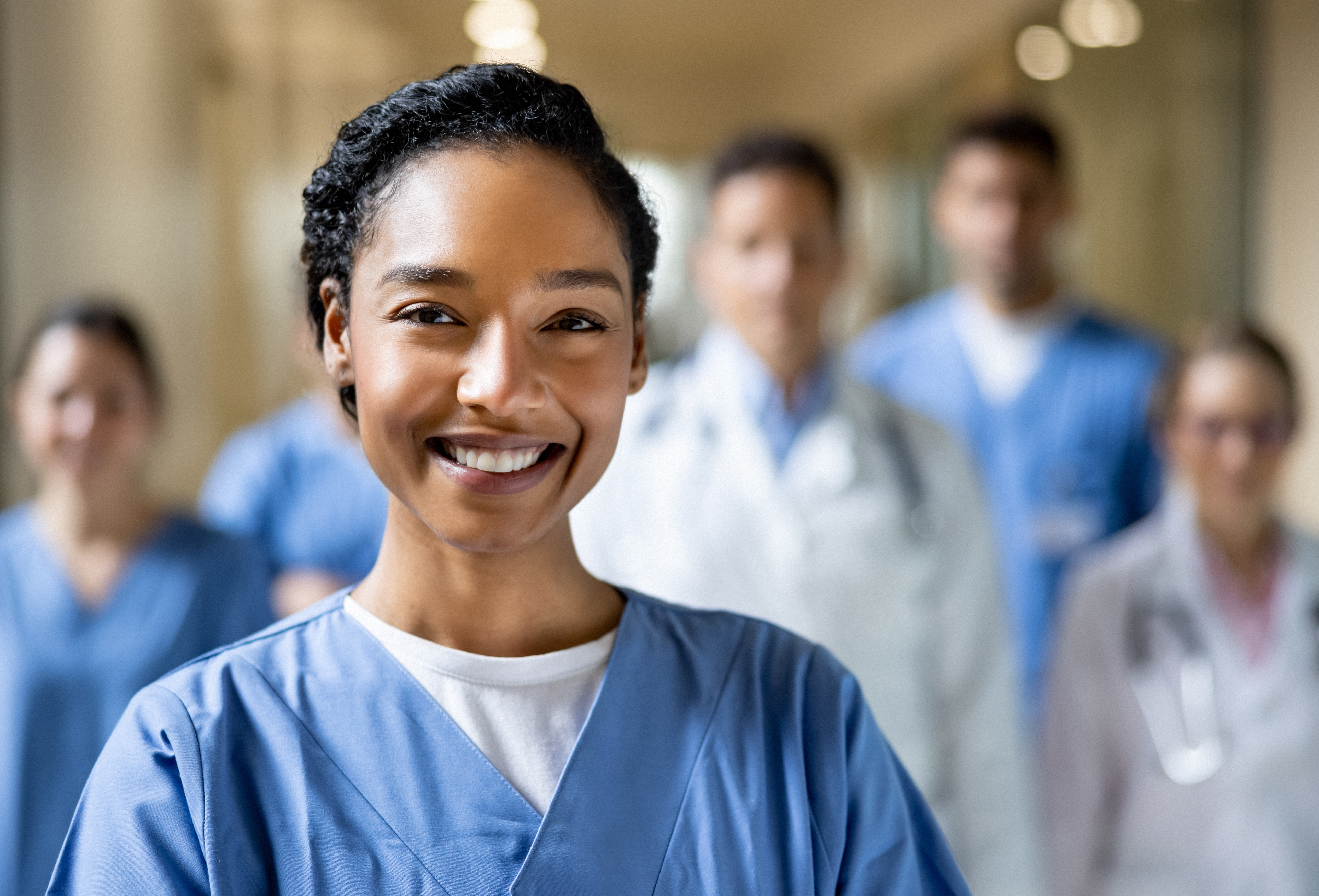 Smiling healthcare professional in blue scrubs with colleagues in hospital corridor