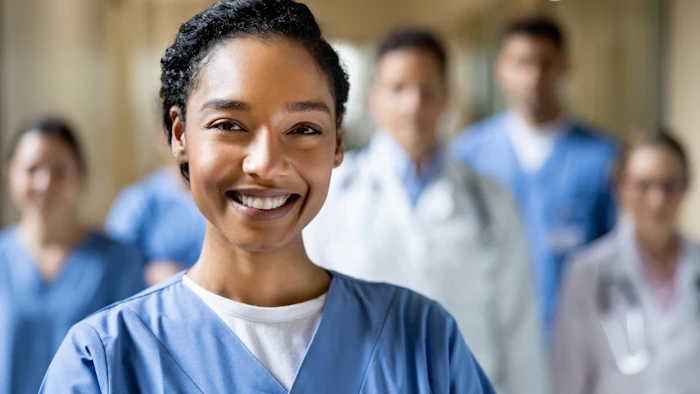 Smiling healthcare professional in blue scrubs with colleagues in hospital corridor