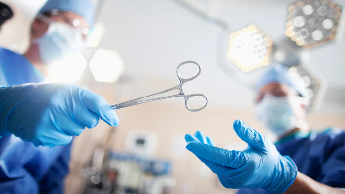 Surgeon in blue gloves holding surgical scissors in operating room with overhead lights and medical equipment