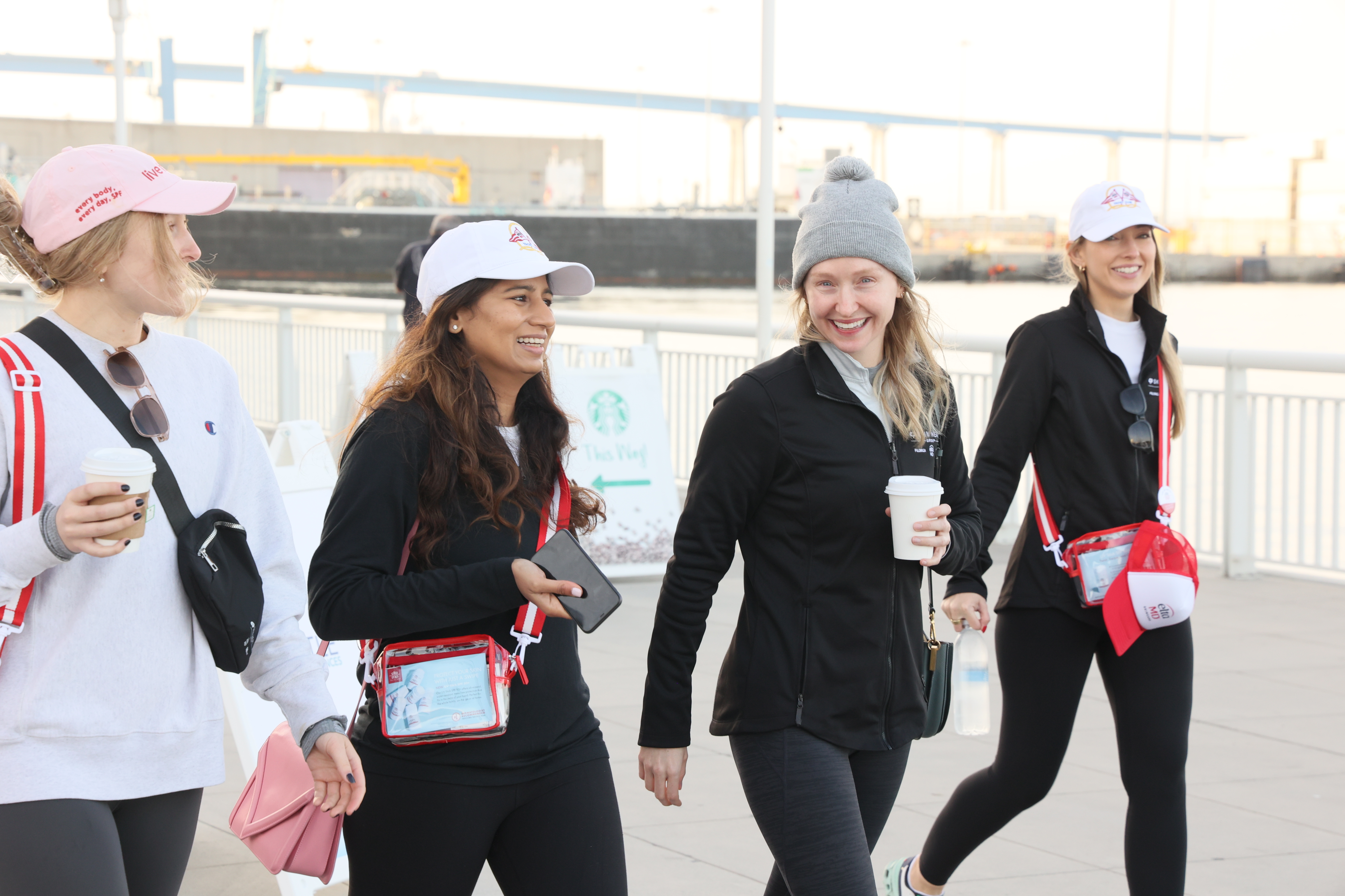 Four women walking together outdoors, wearing branded caps and casual winter clothing