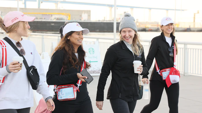 Four women walking together outdoors, wearing branded caps and casual winter clothing