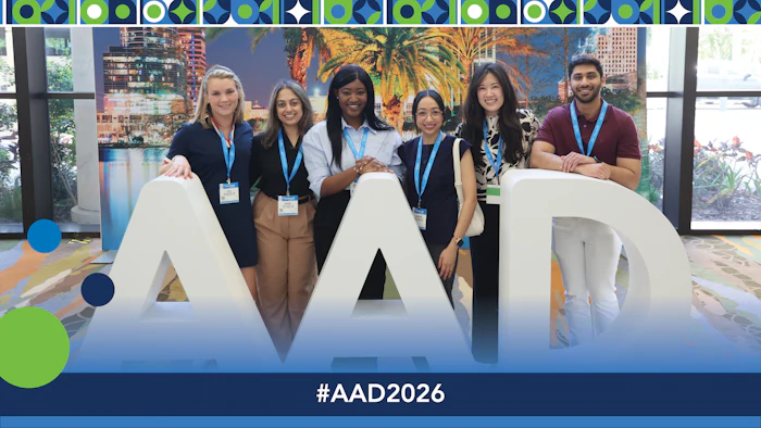 Team of six professionals wearing blue lanyards posing with large AAD letters at conference event