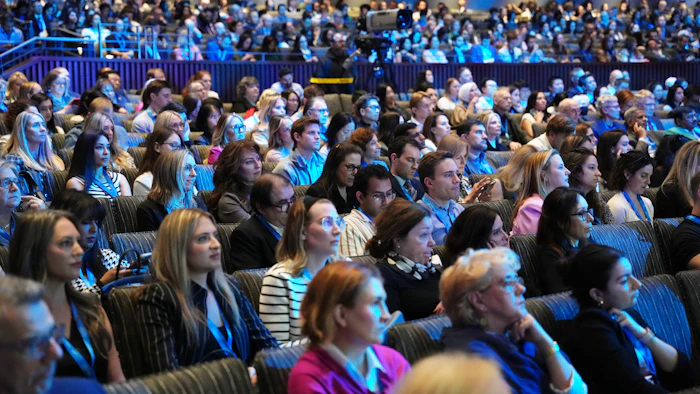 Large diverse audience seated in blue-lit auditorium during corporate event or conference