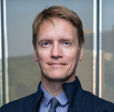 Professional headshot of a man in business attire against an office background