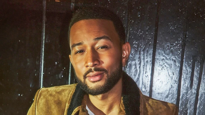 Portrait of a man with beard wearing a mustard-colored jacket against a textured dark background