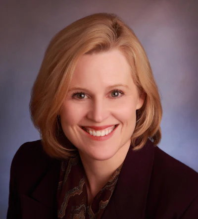 Professional headshot of a smiling woman with auburn hair wearing a dark blazer