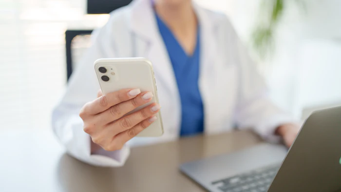Healthcare professional holding white iPhone in medical office with laptop and plants