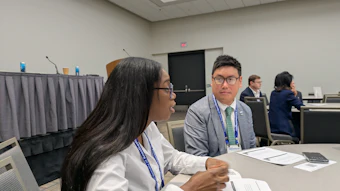 Two professionals wearing conference badges sit at a table during a business meeting or networking event