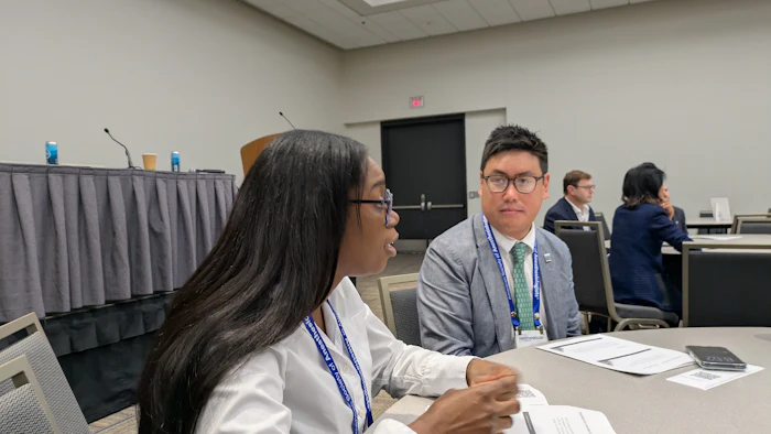 Two professionals wearing conference badges sit at a table during a business meeting or networking event