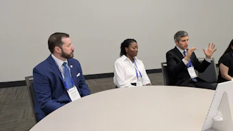 Three professionals in business attire participate in a panel discussion at a conference table with credential badges.