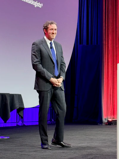 Professional man in gray suit and blue tie speaking on stage at conference event