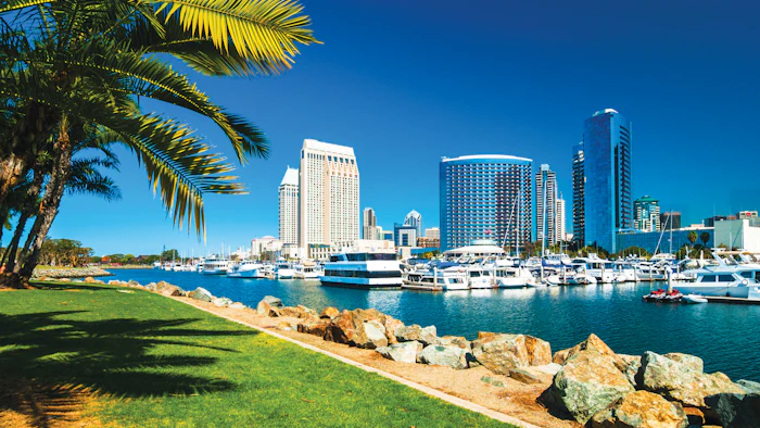 San Diego waterfront with marina, palm trees, green lawn, and downtown skyline under clear blue sky