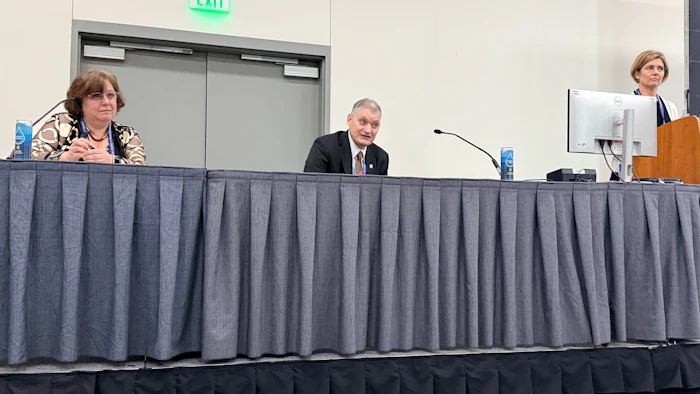 Three panelists seated at a draped table during a professional conference or panel discussion event.
