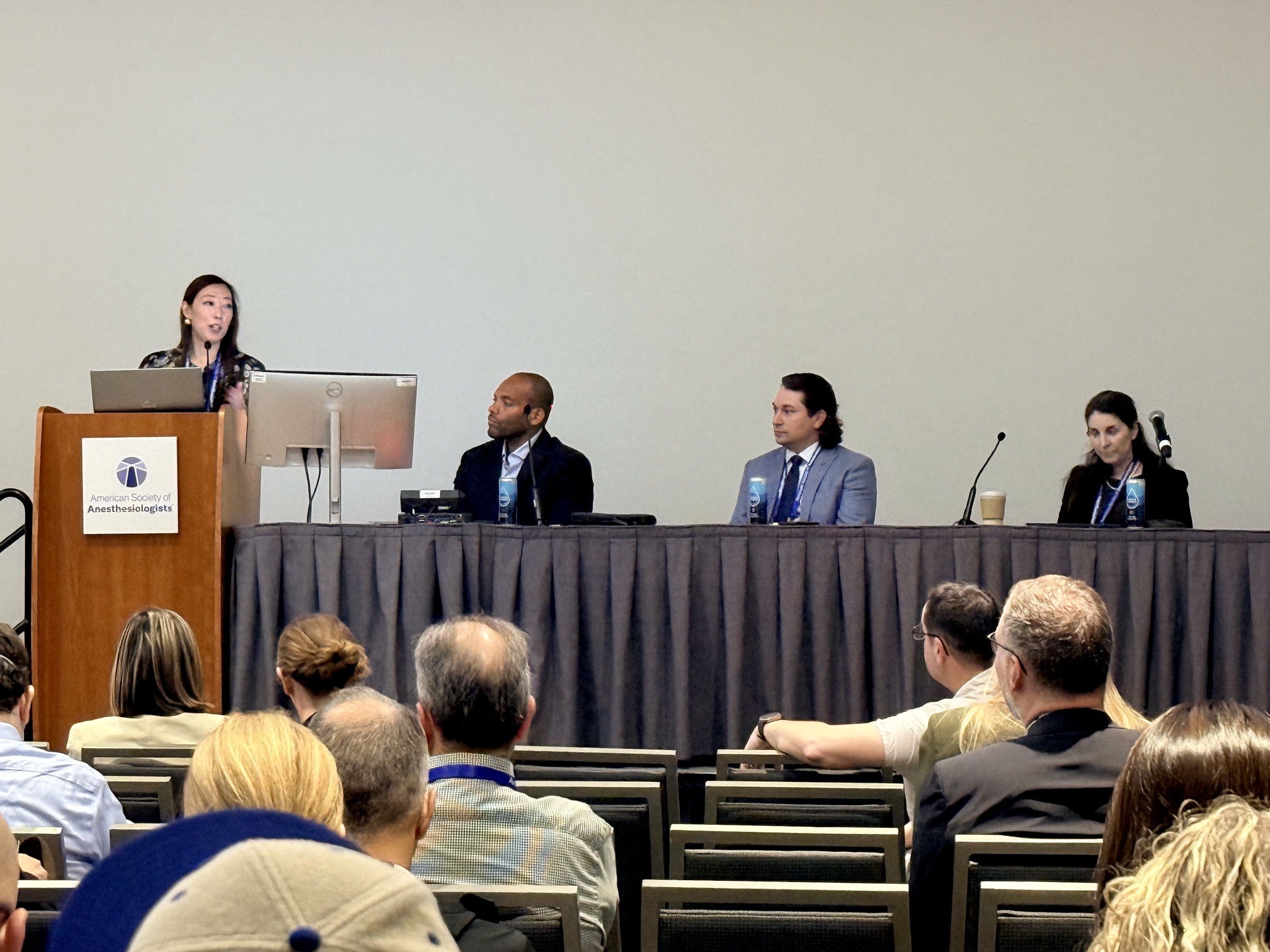 Professional panel discussion with four speakers seated at a table and audience members in foreground at a conference event.