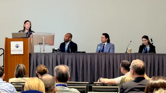 Professional panel discussion with four speakers seated at a table and audience members in foreground at a conference event.