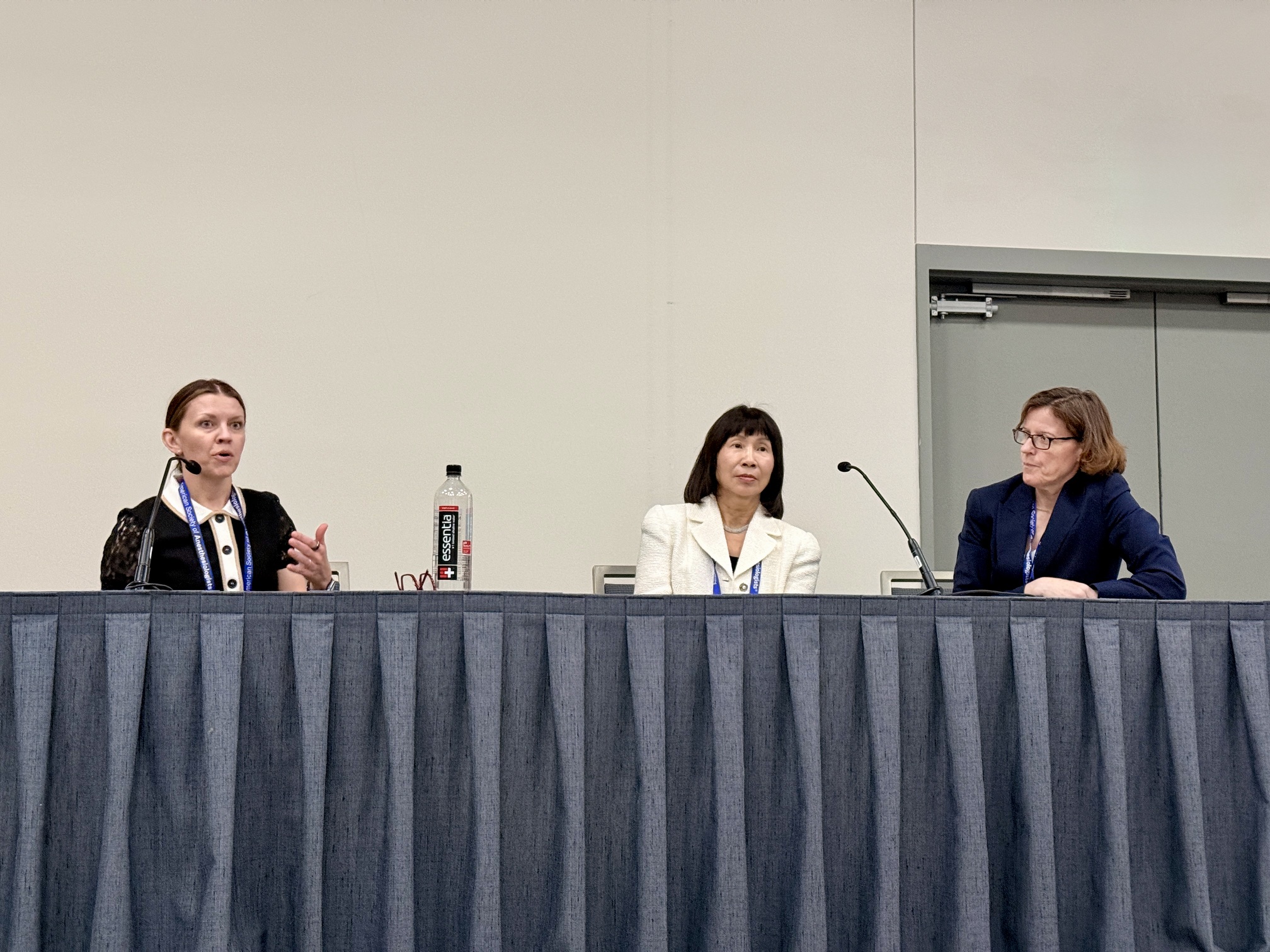 Three professional women panelists seated at a conference table with microphones during a discussion event