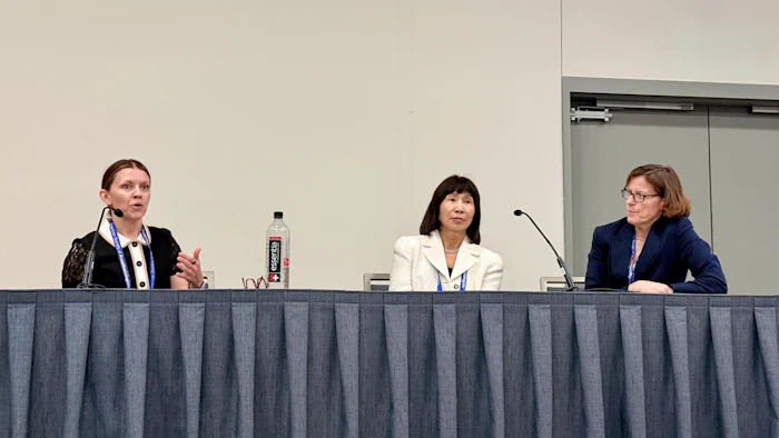 Three professional women panelists seated at a conference table with microphones during a discussion event