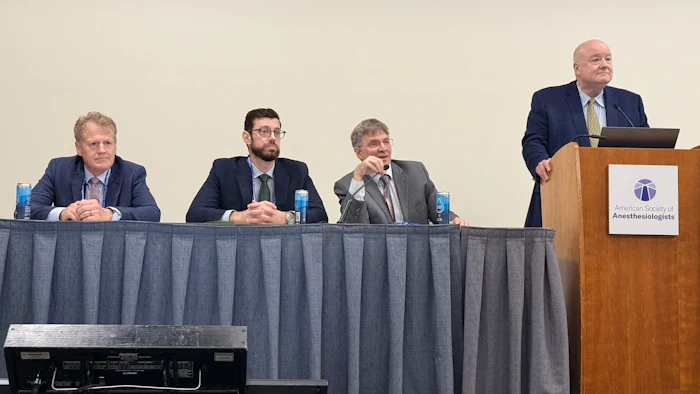 Four professionals at a panel discussion table with one speaker at podium displaying Anesthesiologists organization logo